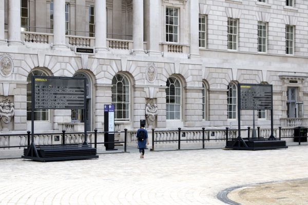 Two boards, one 'arrivals' and one 'departures' are situated in the Somerset House courtyard. a person walks in between them