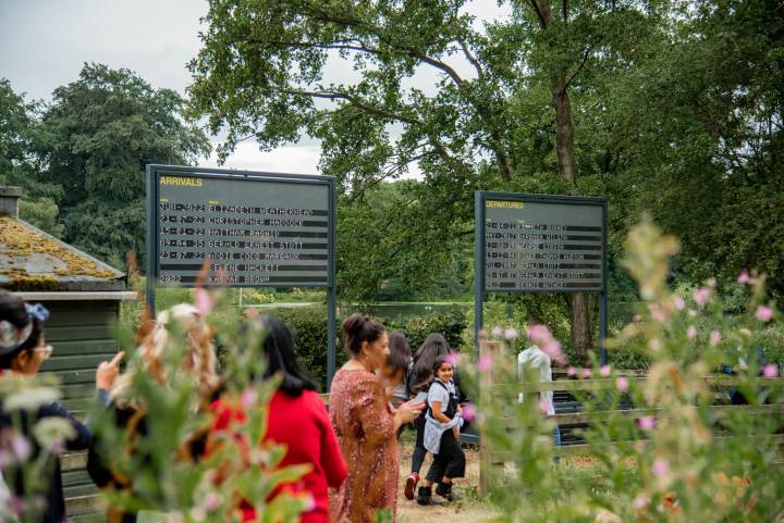 Adults and children play amongst flowers in front of the Arrivals + Departures boards, at Yorkshire Sculpture Park