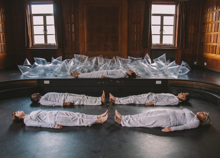 People dressing in matching white outfits lying on the floor of a studio with plastic bags filled with air