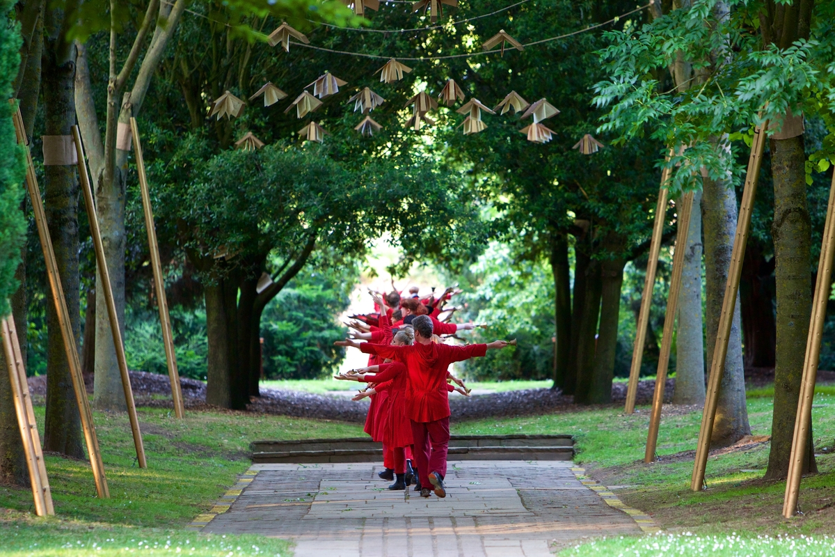 dancers in red walking along a path surrounded by trees