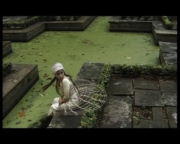 A girl sits with her feet in a pond and turns to look behind her