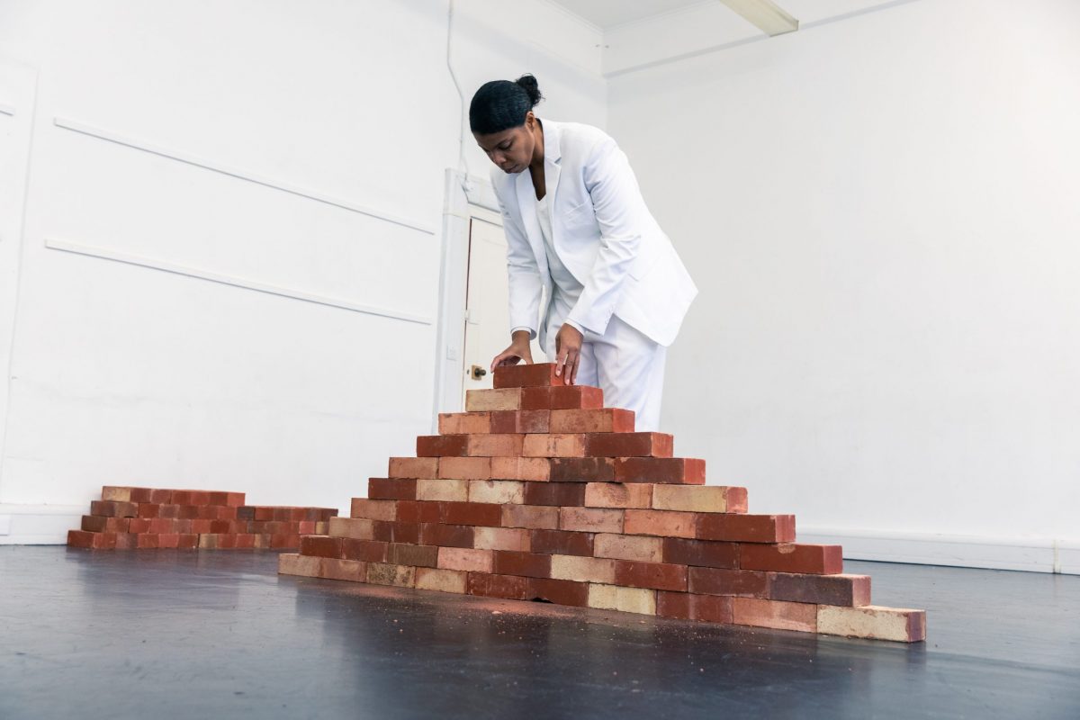 Performer in white suit in studio arranging a stack of bricks