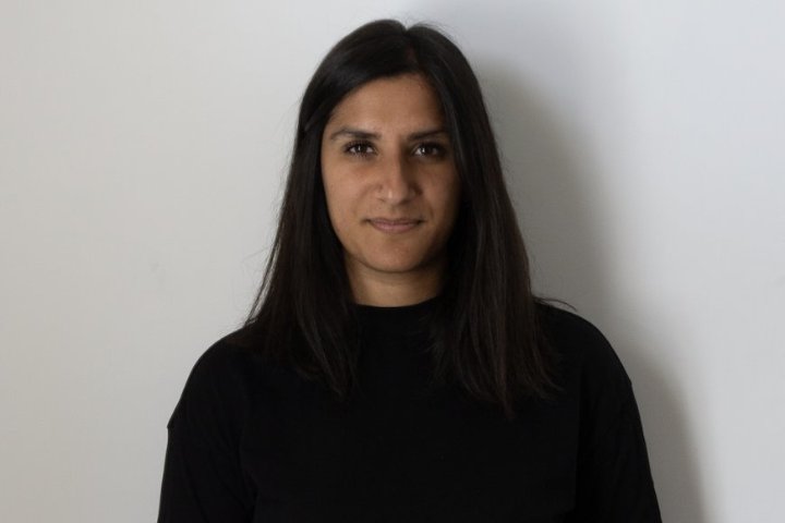 Reena is wearing a black top tucked into black trousers with shoulder length black hair