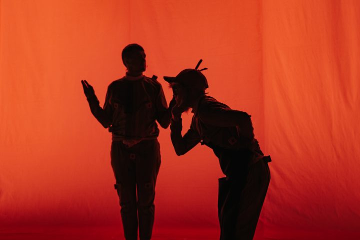 Silhouettes of two people performing against a red backdrop