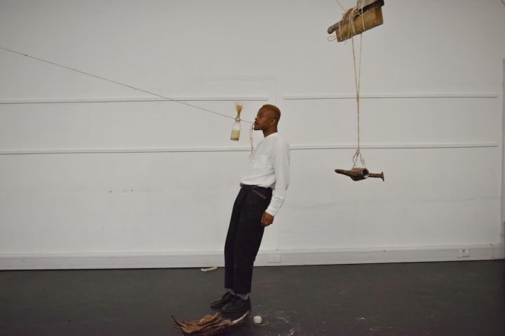 James Jordan Johnson holds a piece of string in his mouth and attached to the string are a bottle, wood and metal implement