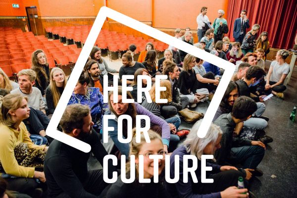 A graphic of Here for Culture overlaid on a photograph of audiences sitting on a stage in a theatre