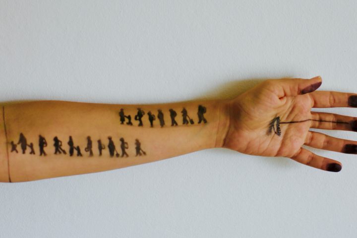 Person's arm stretched out against white background. There are pen drawings of stick people walking across their arm.