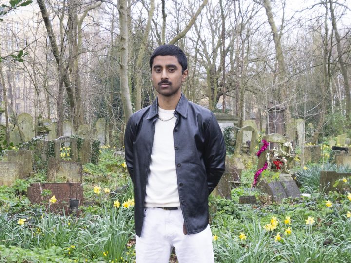 person standing in cemetery wearing black leather jacket, white jumper and white jeans