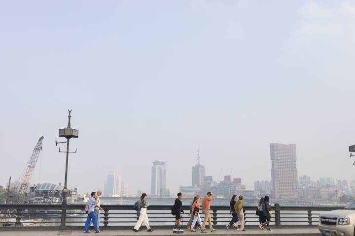 A group of the Another Route fellows walk in ones and twos across a bridge, with the Cairo skyline in the background. The image is in profile, the sky is blue and the air is hazy
