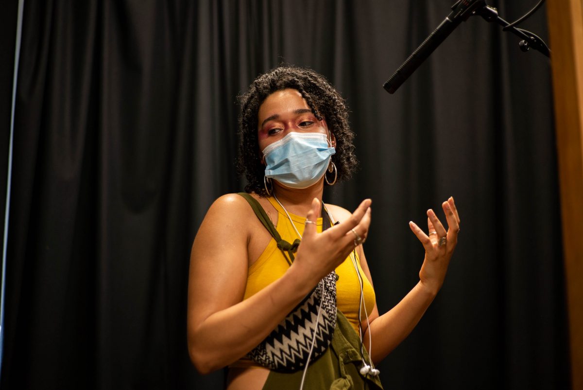 womxn wearing mask speaking with hand gestures. A mic is overhead.