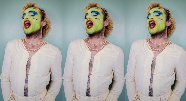 person with green face paint and valour written on their cheek, wearing necklaces, posing with their mouth open