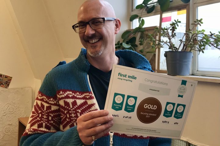 David Titmuss, smiling into the camera, holding a certificate for the first mile easy recycling. David is bald, wearing glasses and wearing a blue knitted cardigan.