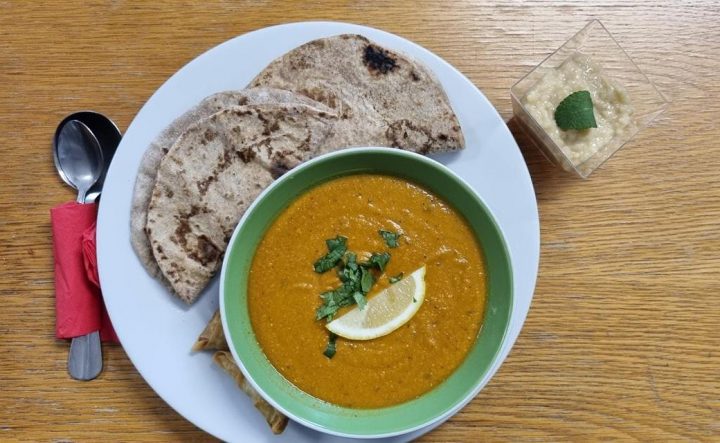 bowl of harissa soup with lemon and parsley garnished on top with chapati bread on the side