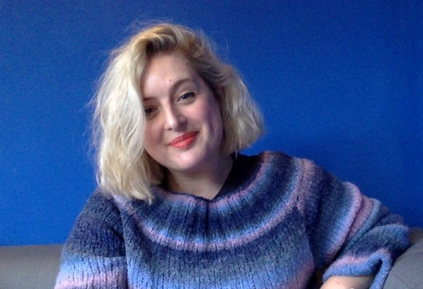 Image of Cat Harrison, woman with short blonde hair wearing red lipstick and blue and purple knitted jumper smiling into the camera