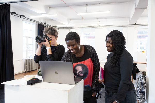 Three people stand behind a laptop, one holds a camera up