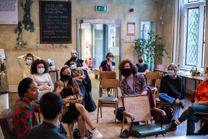 people sitting in a cafe talking, they are spaced out and wearing masks