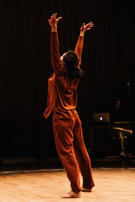 behind view of person dancing in a spotlight with their arms up expressively