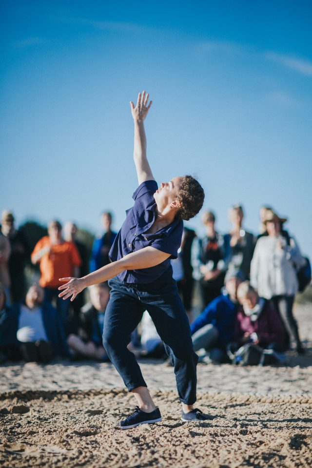 person dancing inside a circle shaped rope on sandy shore with an audience