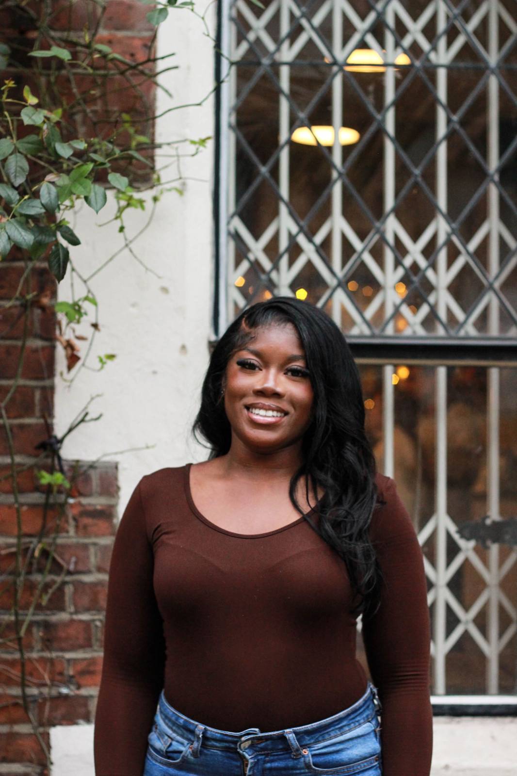 portrait of Helen, a black woman wearing a long sleeved brown top and smiling into the camera