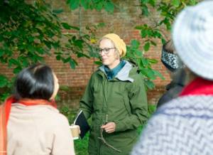 Rosemary Lee smiling to a small group of people. Rosemary wearing glasses a yellow hat loosely on her head.