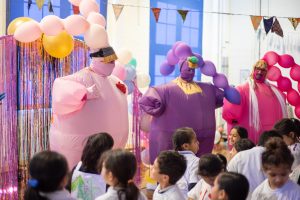 three people in blown up balloon alien costumes, performing in front of school children