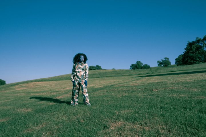 person painted blue wearing floral shirt and trousers, standing in a field