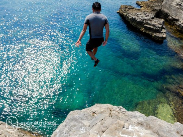 A shot of Medz jumping off a cliff into a clear blue sea.