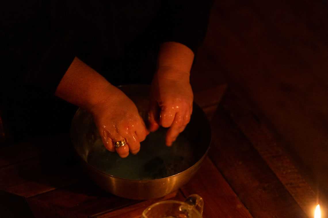 A guest washes their hands in a bowl of water, lit by candlelight 