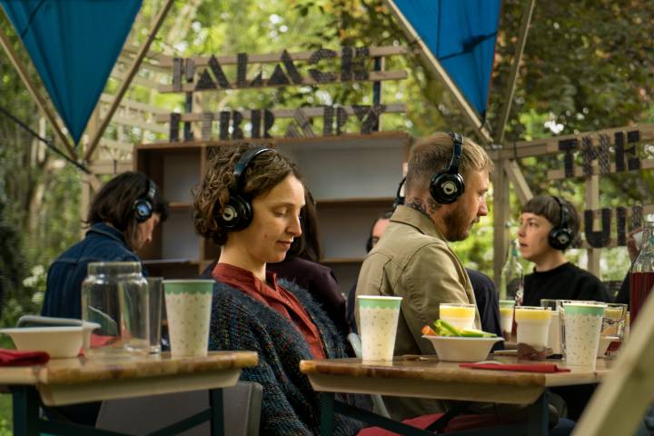 A group of people sitting within The People's Palace of Possibility, wearing headphones and eating food
