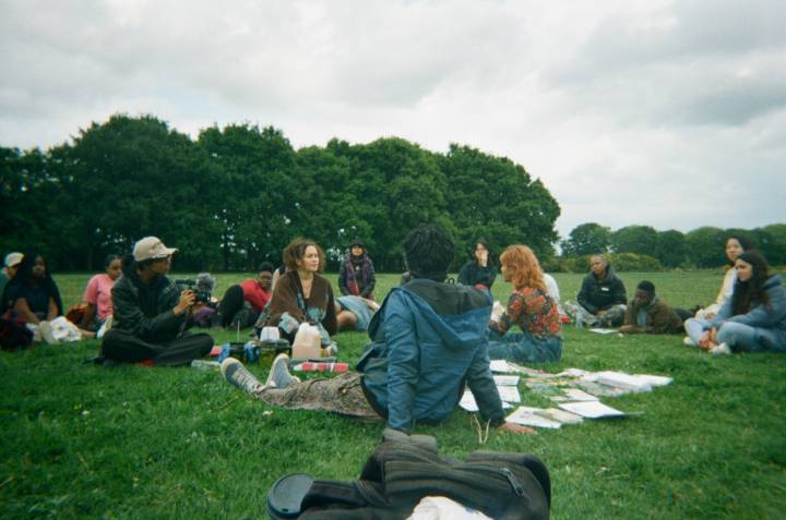 A group of QTIBPOC people participate in a workshop, sitting in a grassy, open space