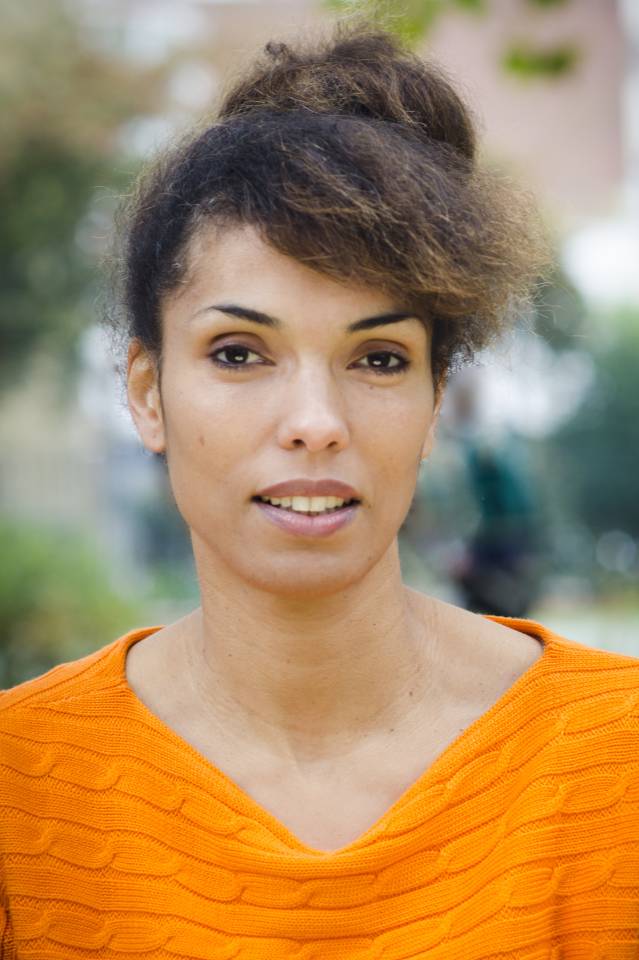 An image of artist Zoe Laureen Palmer, looking directly into the camera from shoulders up, and wearing an orange top