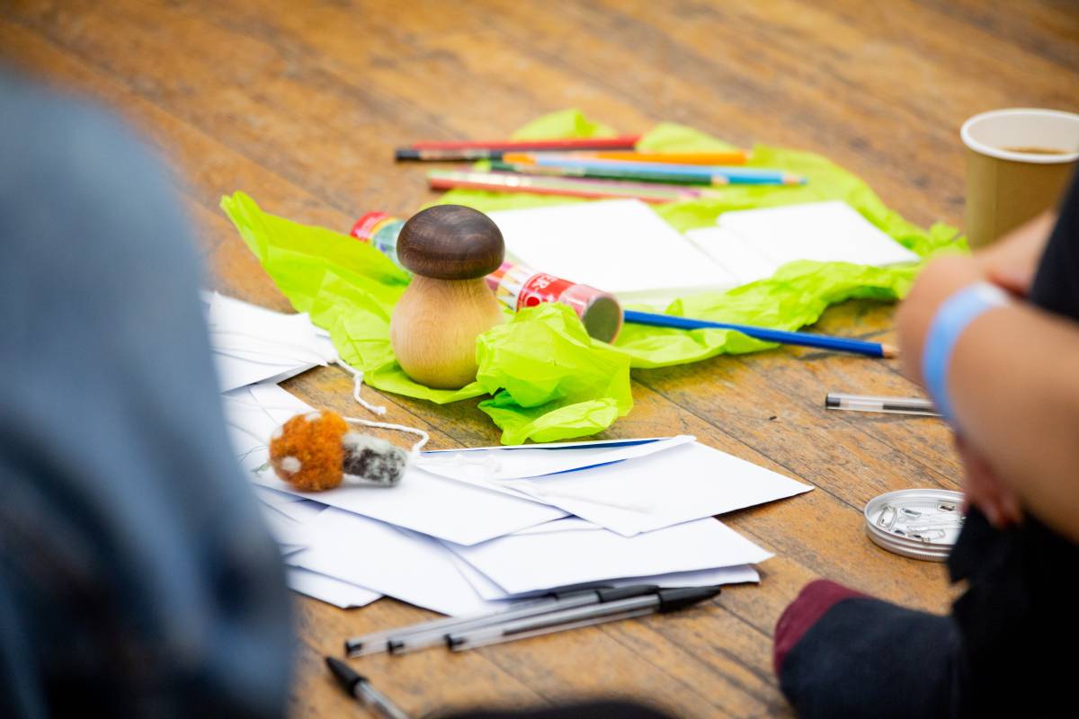 A photo of objects placed on a wooden floor - a wooden mushroom, paper, pens, tissue paper