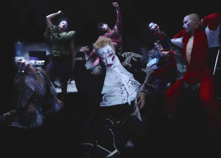 An image of BULLYACHE cast performing TOM. They make gestural. dramatic poses, wearing trashy, beaded, glamorous costumes. They have clownish makeup and moody expressions