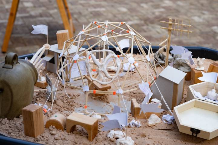 A photo of a wooden model in a sandbox, displaying lots of clay figures of speculative future living scenarios
