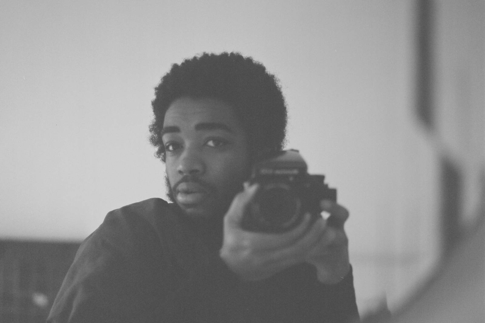 A black-and-white selfie style photo of artist Abel (they/them), holding the camera gently next to their face and looking into the mirror