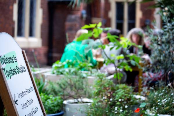 A photo of the plants and tables outside Toynbee Studios, with a sign reading 'Artsadmin, Toynbee Studios'