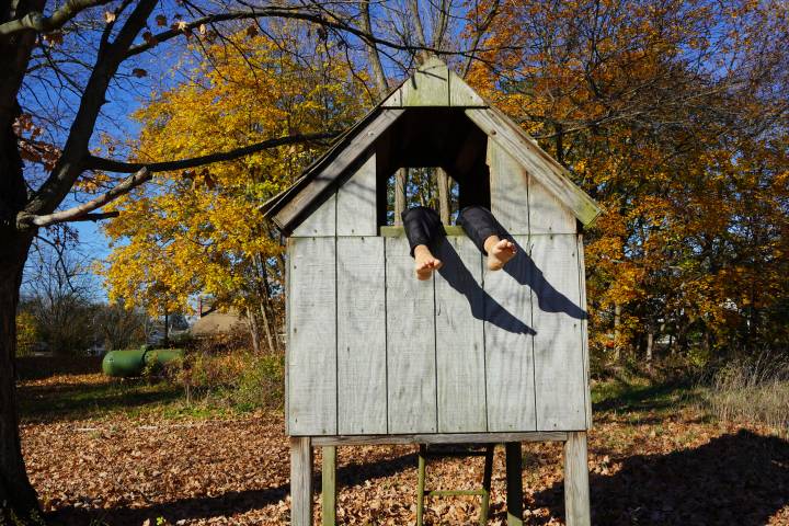 A photo of a giant birdhouse, with a pair of barefoot human legs poking out