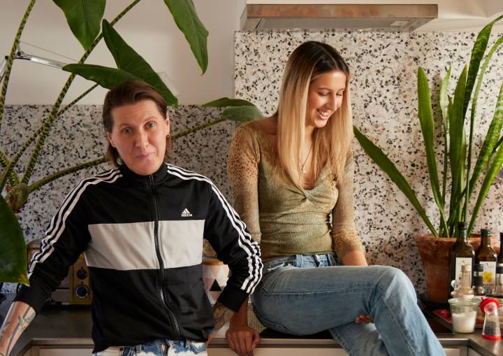 A photo of Tink Flaherty and their daughter Abra Flaherty sitting in their kitchen at home, smiling and laughing