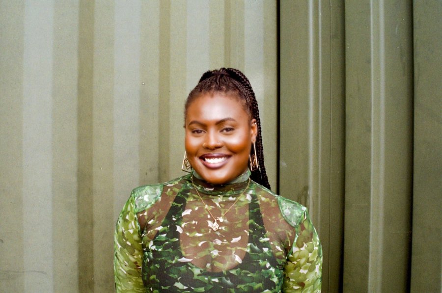 A photo of Tobi Kyeremateng, looking at the camera and smiling, and wearing a green patterned top