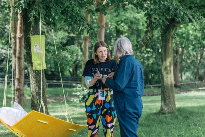 A photo of a brightly dressed volunteer speaking to an audience member at a festival